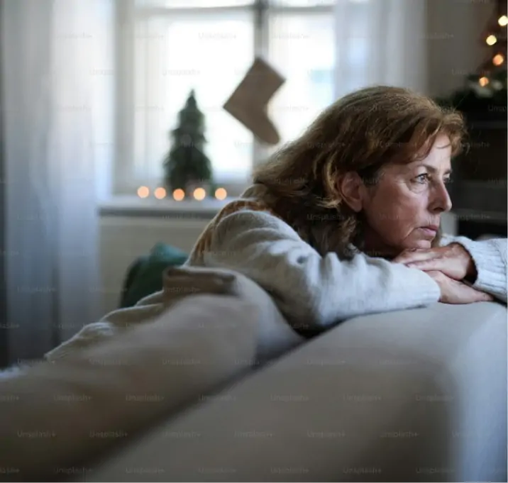 A woman with dementia sits on a sofa and looks out the window.