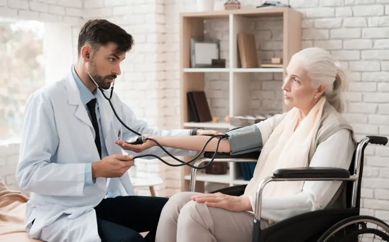 Male doctor examining female dementia patient sitting in wheelchair at home